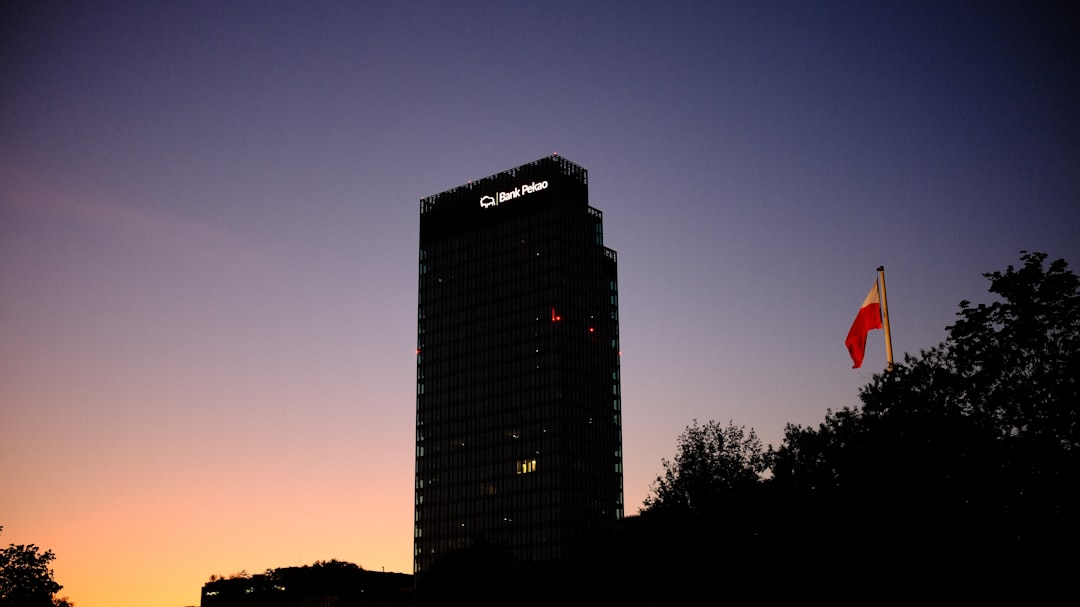 A serene view of Warsaws Forest skyscraper (120 m) housing Bank Pekao, with the Maszt Wolności flagpole proudly displaying Polands white and red flag. Captured during the soft hues of a summer sunset, this image blends modern architecture with national pride.